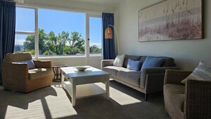 A living room with a sofa, armchairs, a coffee table, and a large window with curtains. - Bay Getaway 2 Bedroom apartment (Timaru)