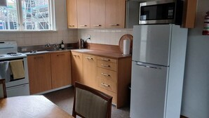 Una cocina con armarios de madera, un microondas de acero inoxidable, un refrigerador blanco y un ventanal con vistas a una construcción.