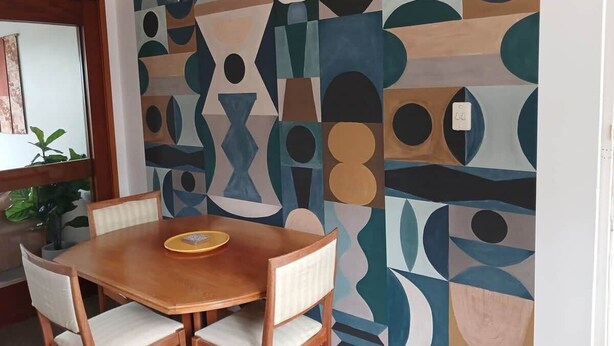Un comedor con una mesa y sillas de madera, un muro con diseño y una planta en maceta.