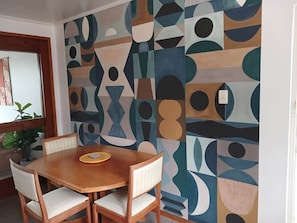 A dining area with a wooden table and chairs, a patterned wall, and a potted plant.