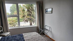 Una habitación de hotel con una cama, una ventana con cortinas, una silla y un cuadro en la pared.
