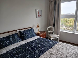 A bedroom with a bed, a nightstand, a chair, a window, and a framed picture on the wall.