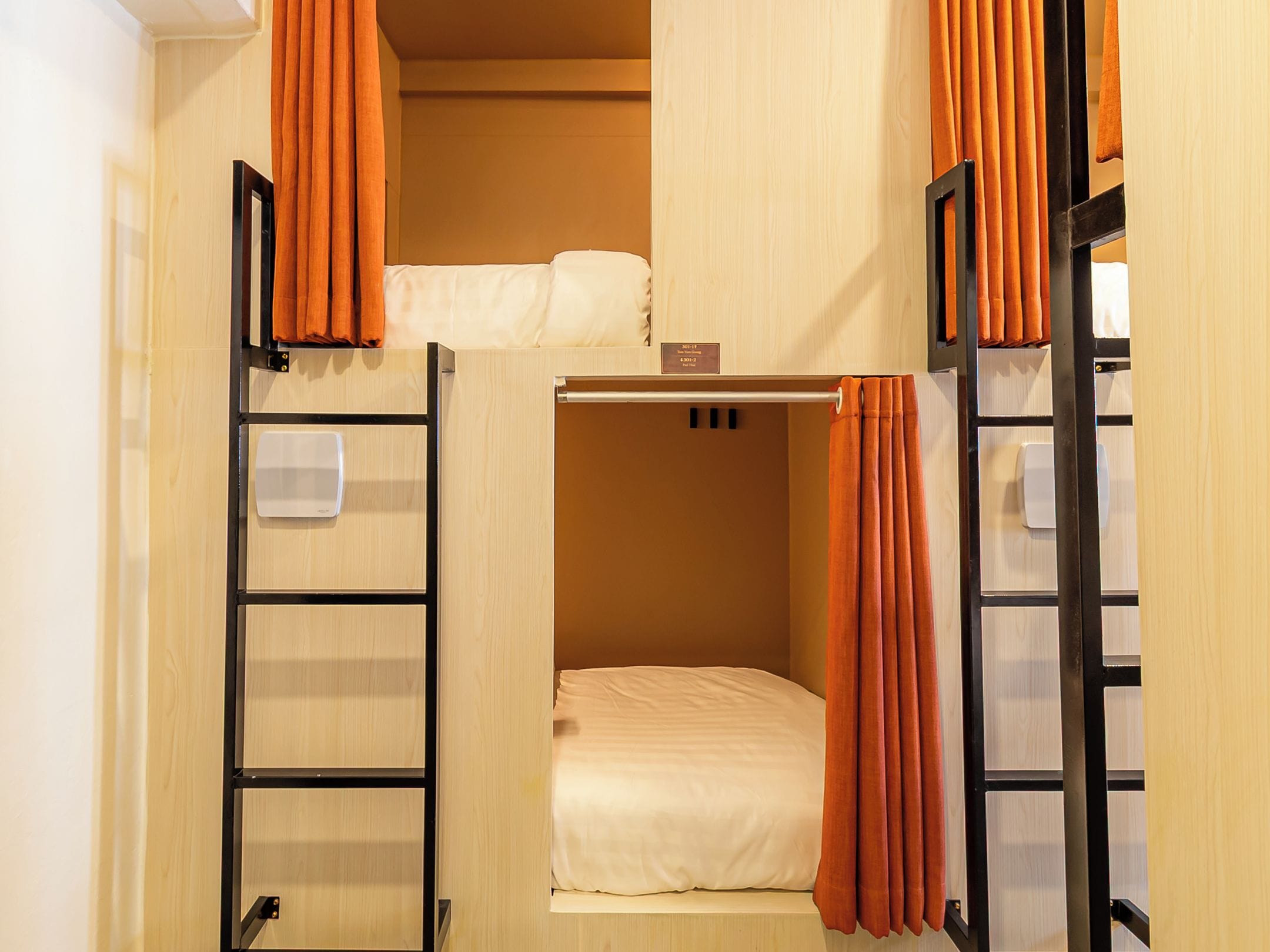 Een kleine kamer met stapelbedden, een klein nachtkastje en oranje gordijnen.