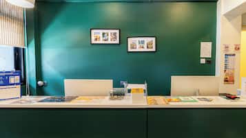 A reception desk with a green wall, framed pictures, a calendar, a tipbox, and a train ticket booking service poster.