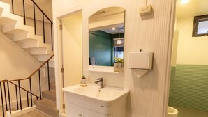 Casa de banho com lavatório branco, espelho, sanita e parede verde.