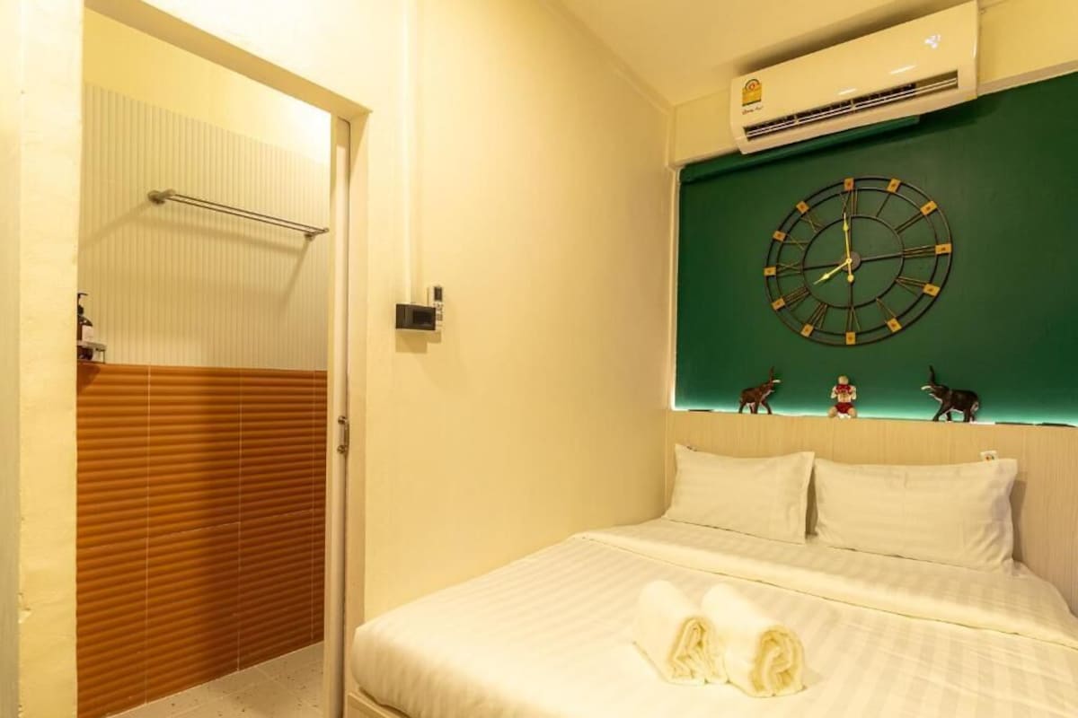 A hotel room with a bed, a wall-mounted clock, and a towel on the bed.