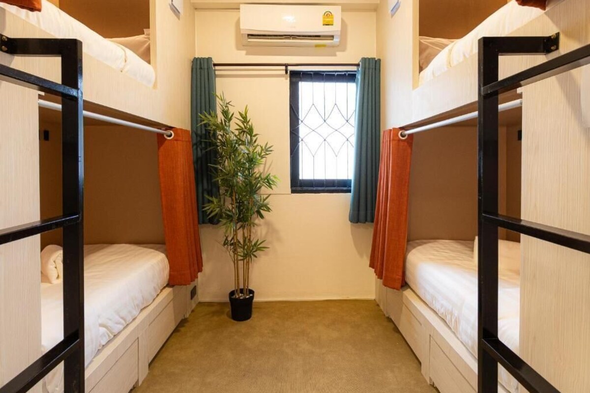 Ein kleines Zimmer mit Etagenbetten, einem Blumentopf, einer Klimaanlage und einem Fenster mit Vorhängen.