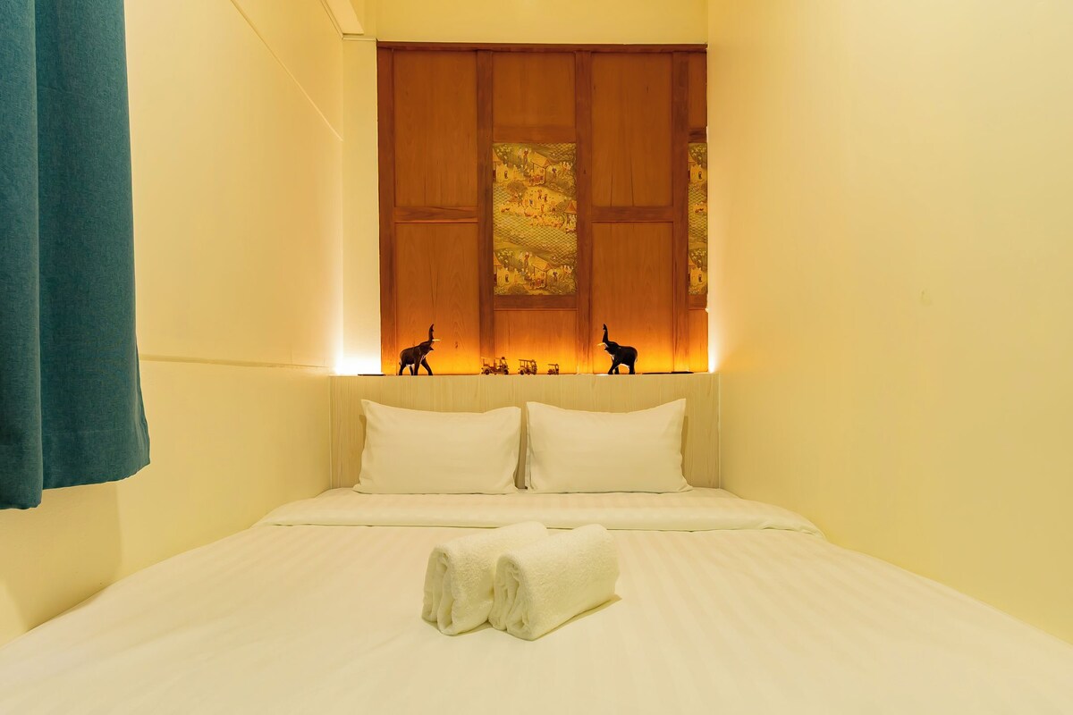 A hotel room with a bed, pillows, a folded towel, and a decorative wall panel with figurines.
