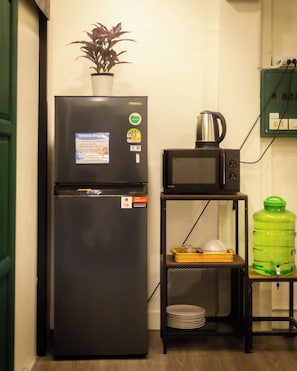 Una kitchenette compacta con refrigerador, microondas y un pequeño estante con tetera y platos.
