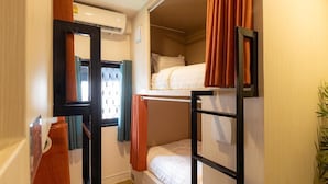 Une chambre avec un lit superposé, une fenêtre, un miroir et une plante.
