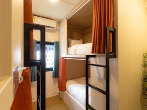 Ein Mehrbettzimmer mit Fenster, Spiegel und Pflanze.