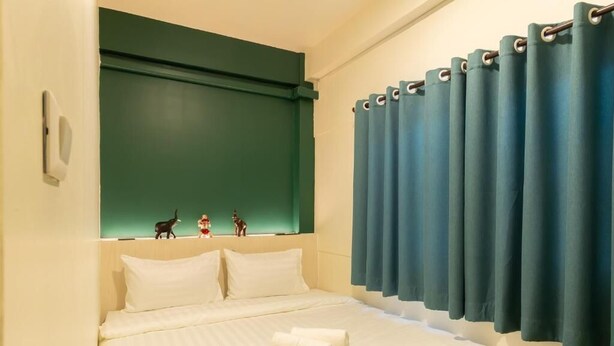 Une chambre d’hôtel avec un lit, une tête de lit, une fenêtre avec des rideaux et un luminaire fixé au mur.