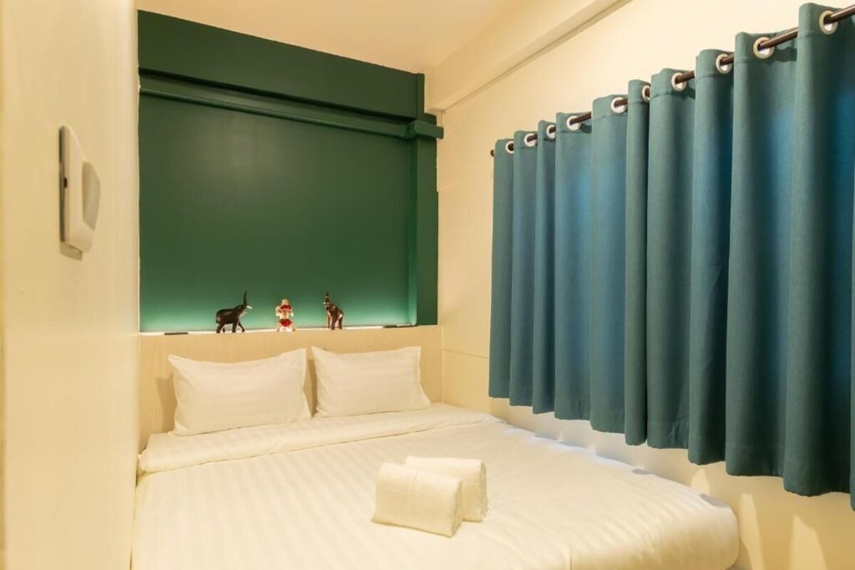 Ein Hotelzimmer mit einem Bett, einem Kopfteil, einem Fenster mit Vorhängen und einer Wandleuchte.
