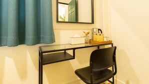 Quarto com escrivaninha preta, cadeira, espelho e janela com cortinas.