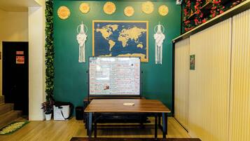 A room with a green wall, a world map, a whiteboard with a schedule, a wooden table, and a black trash bin.