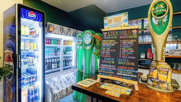 A bar area with a Pepsi refrigerator, a Chang beer tap, and a chalkboard menu listing cocktails and prices.