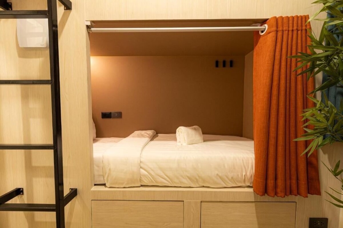 Ein Einzelbett mit Kopfteil, einem kleinen Nachttisch und einem Vorhang.