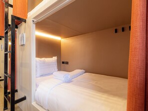 A single bed with white bedding in a room with beige walls and a wooden door frame. -  Social Pod Khao San Hostel (Bangkok)