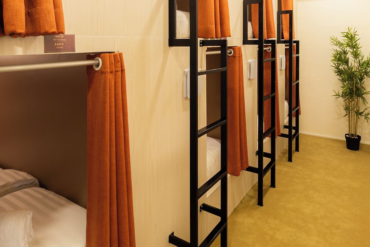 A hotel room with bunk beds, orange curtains, a potted plant, and an air conditioning unit.