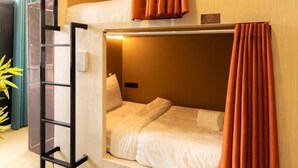 Une chambre avec un lit superposé, des rideaux orange, une échelle et une petite étagère.