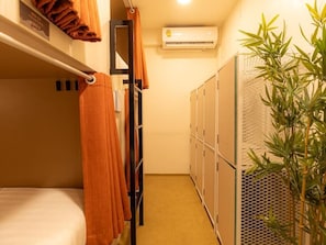 A compact hotel room with bunk beds, a small plant, and a wall-mounted air conditioner. - Social Pod Khao San Hostel (Bangkok)