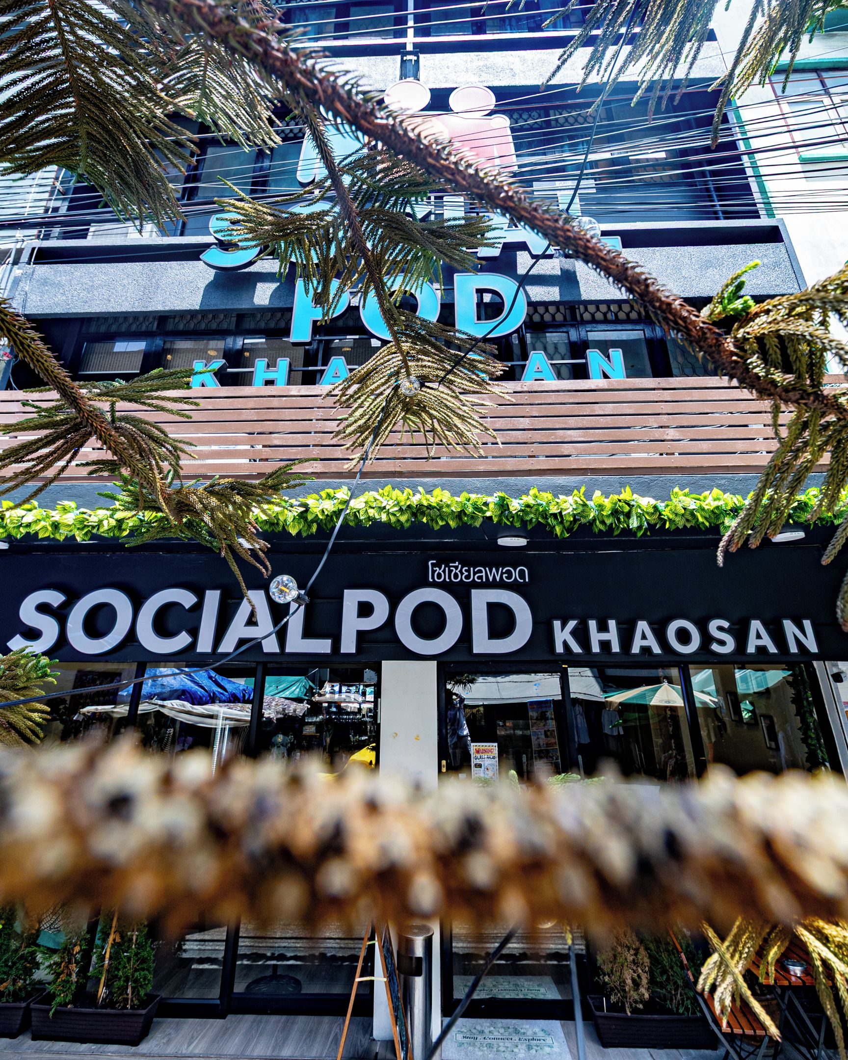A building with a sign that reads 'SOCIAL POD KHAOSAN' and a view of the interior through the windows.