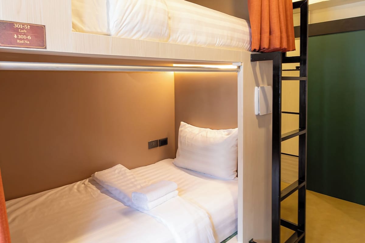 A bunk bed room with a ladder, a sign indicating room numbers, and a curtain.