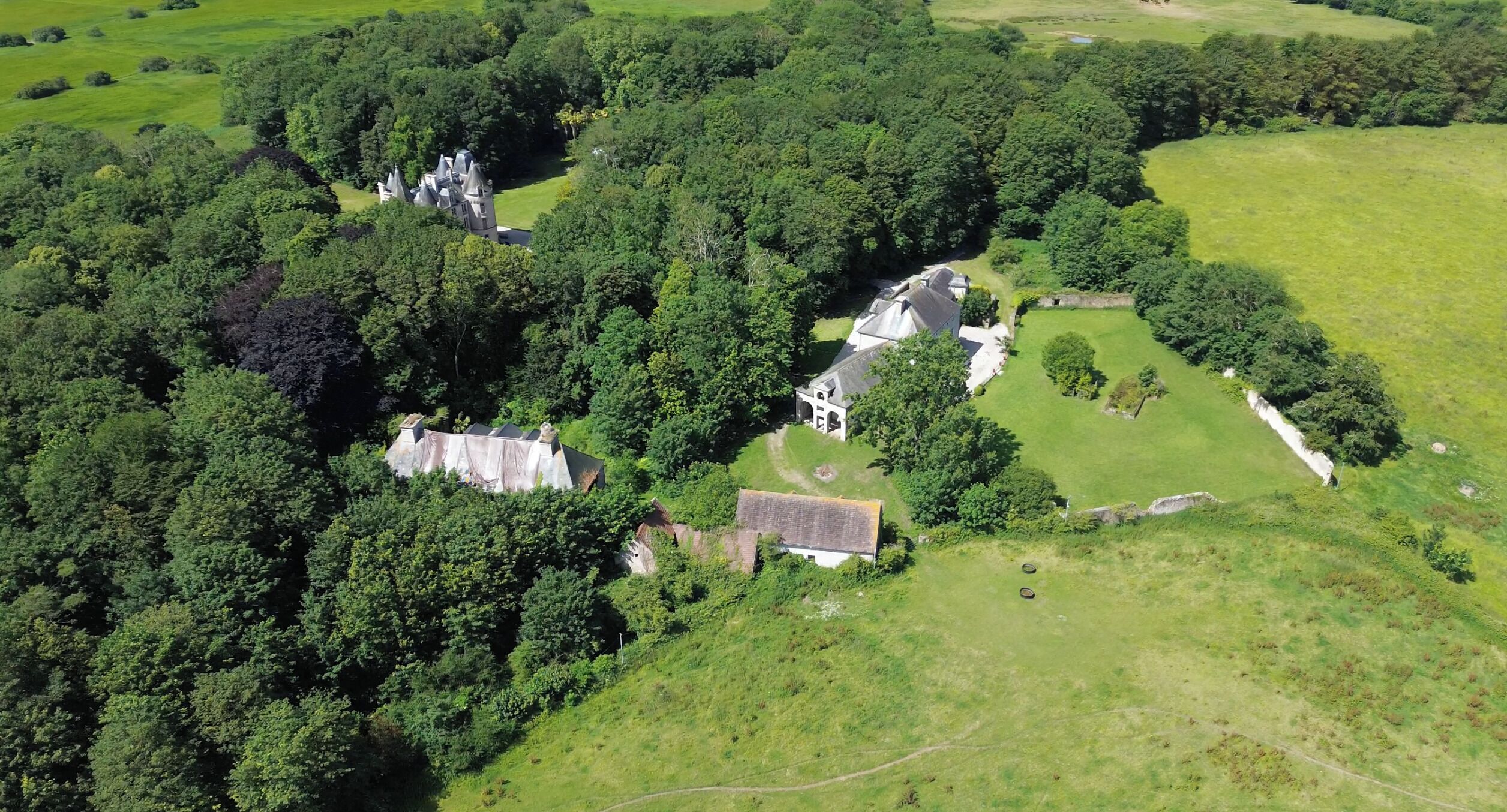 An aerial view of a property with multiple buildings surrounded by dense greenery.