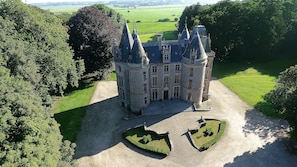 Un château doté d’une tour centrale, entouré d’une végétation luxuriante et d’une pelouse bien entretenue.