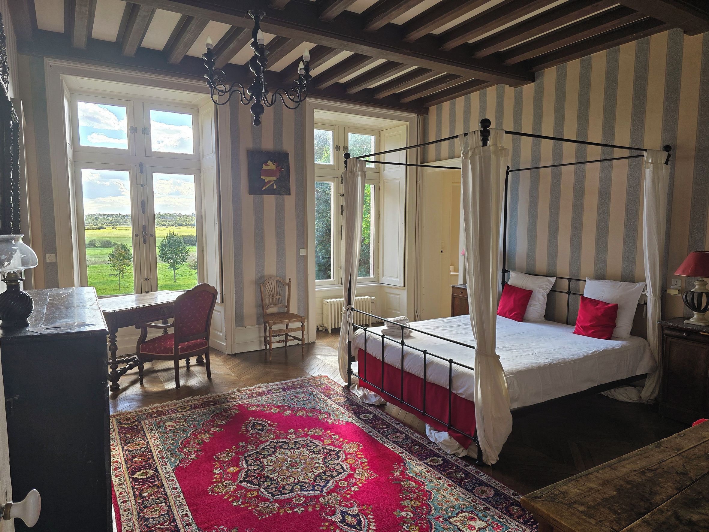 Une chambre à coucher avec un lit à baldaquin, un bureau avec une chaise et une grande fenêtre.