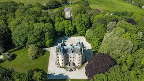 A large, historic building with multiple towers and a central courtyard, surrounded by dense greenery.