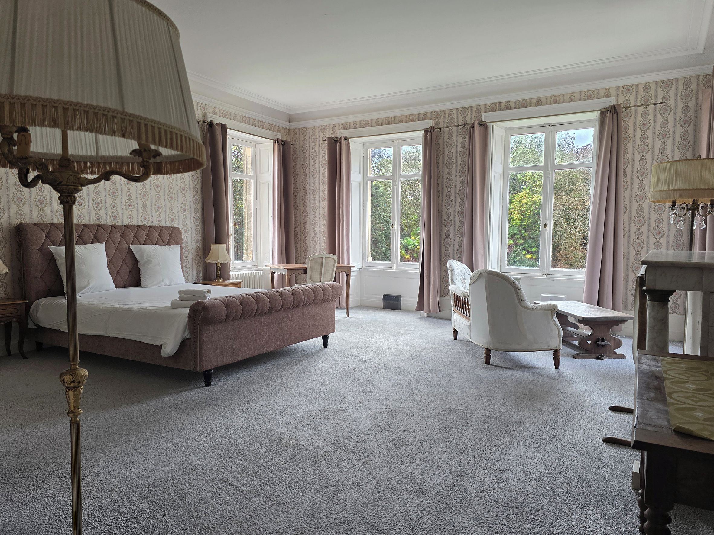 A hotel room with a bed, a chair, a table, and large windows.