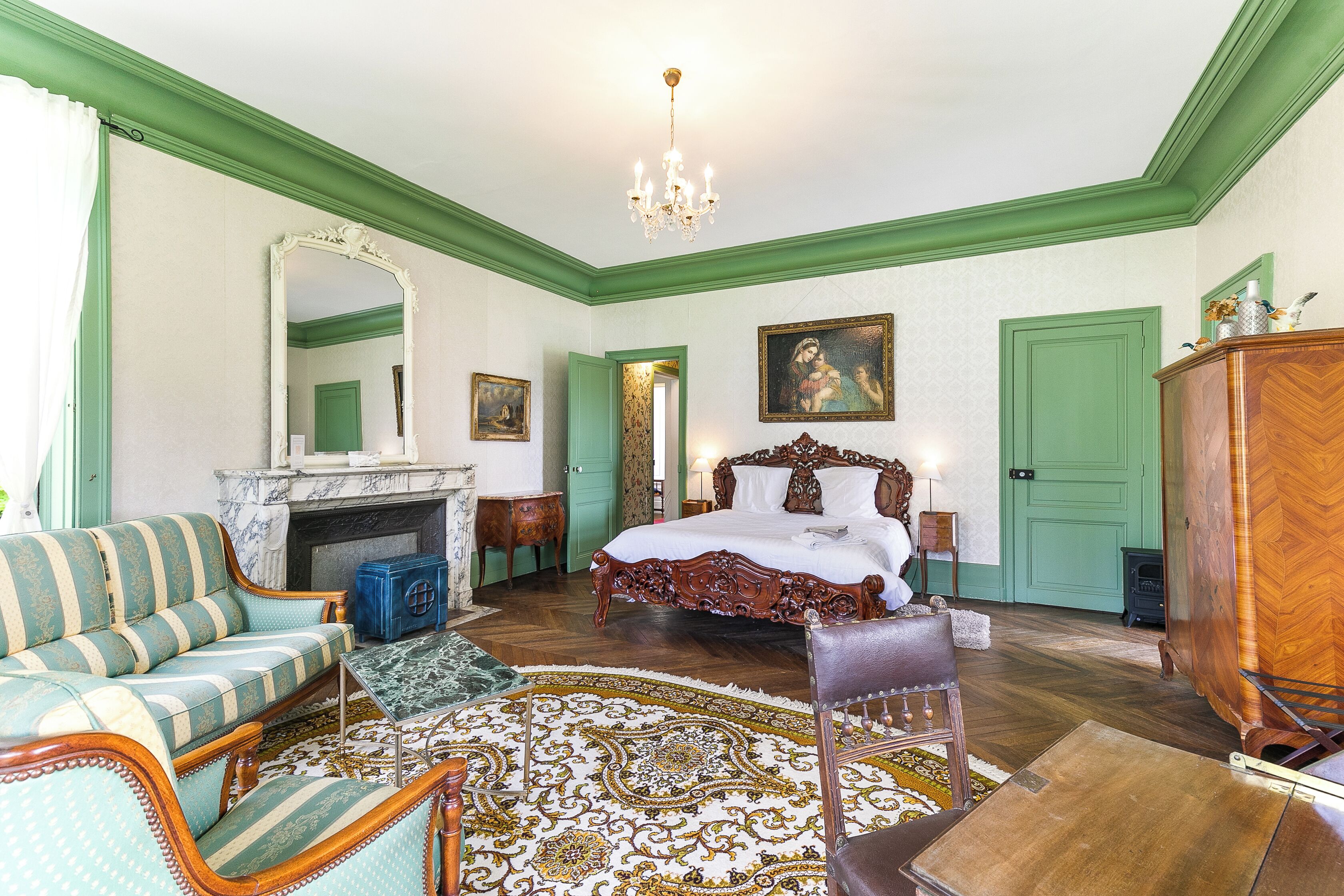 A room with a large bed, a sitting area with a sofa, a fireplace, and a chandelier.