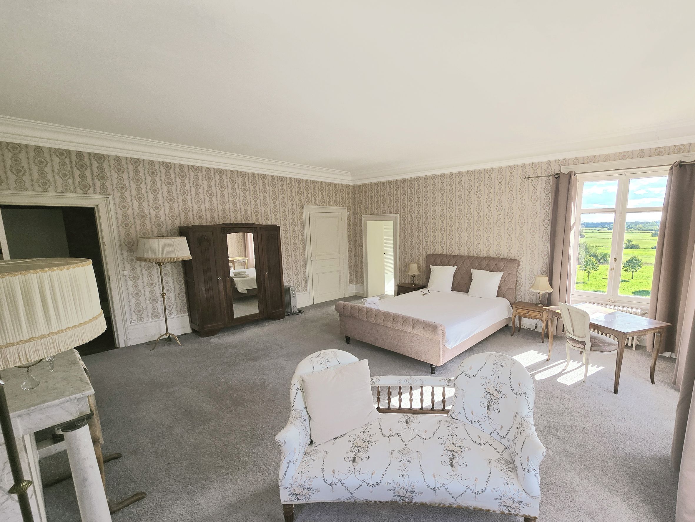 A bedroom with a large bed, a chair, a desk, and a view of the outdoors.