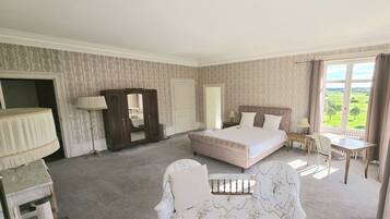 A bedroom with a large bed, a chair, a desk, and a view of the outdoors.
