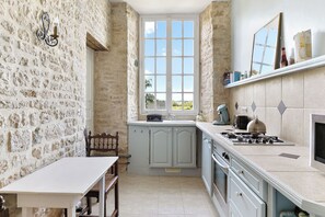 A kitchen with stone walls, a window, a stove, and a dining area.