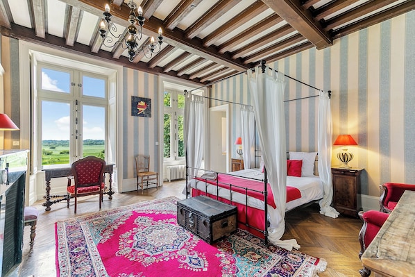 A room with a four-poster bed, a large window, and a view of the outdoors.