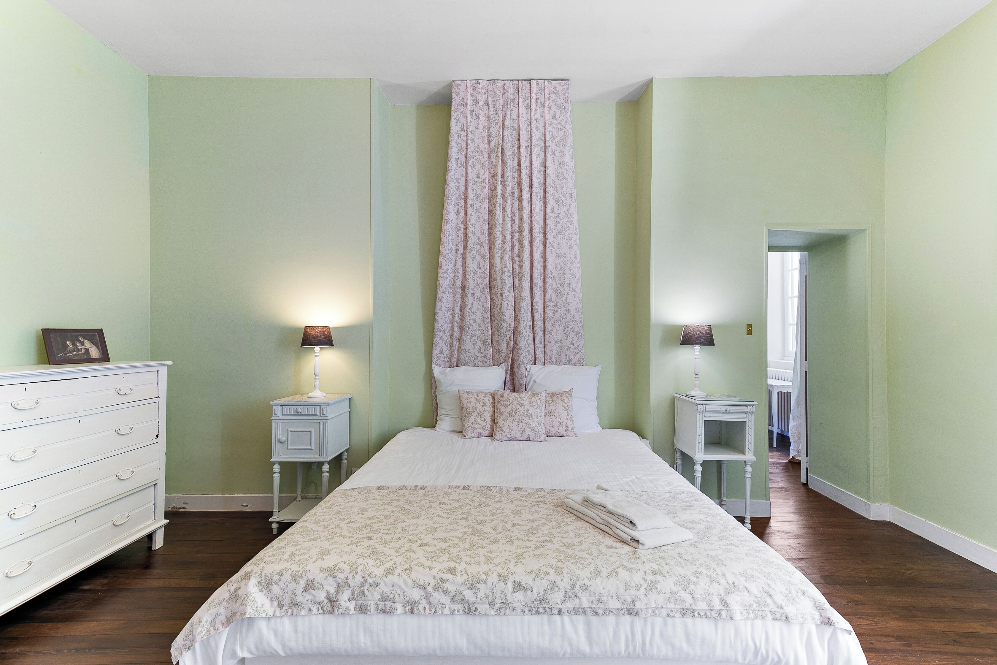 Un dormitorio con una cama grande, dos mesitas de noche, un aparador y una puerta que da a otra habitación.