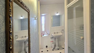 Ein Badezimmer mit großem Spiegel, zwei Waschbecken, einer Dusche und einer Toilette.