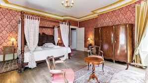 A four-poster bed with a canopy, a wooden wardrobe, a small round table, a chair, and a chandelier. - Château de l'Isle Marie (Picauville)
