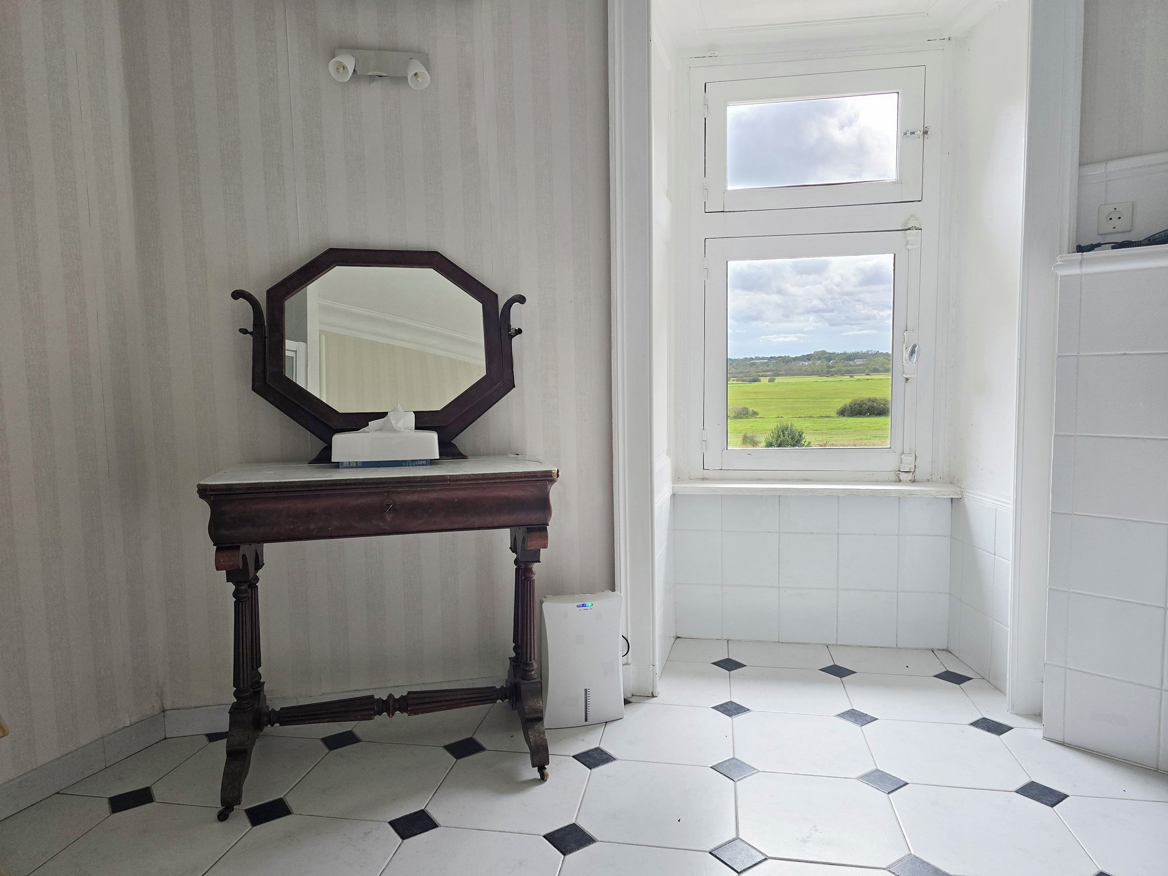 A bathroom with a large mirror, a small table, and a window with a view of a green landscape.