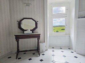 Ein Badezimmer mit einem großen Spiegel, einem kleinen Tisch und einem Fenster mit Blick auf eine grüne Landschaft.