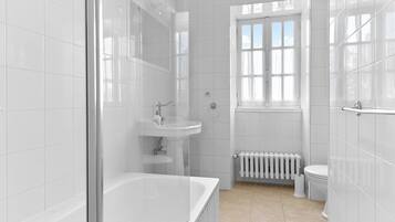 A modern bathroom with white tiles, a bathtub, a sink, a toilet, and a window.