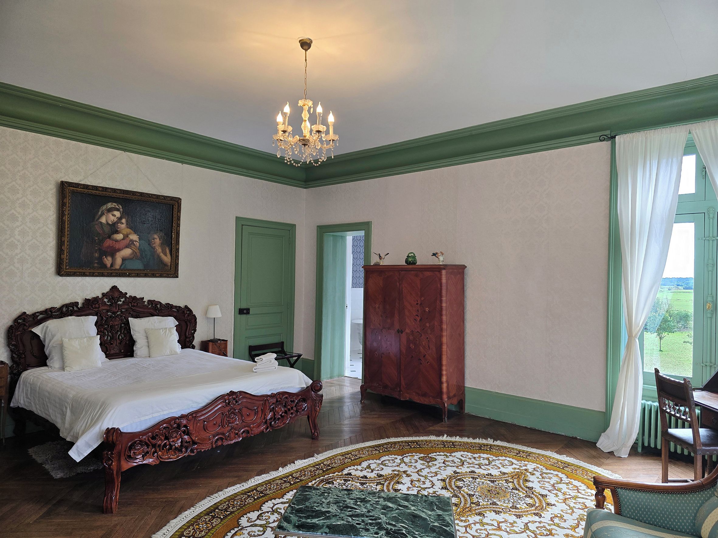 Une chambre à coucher avec un grand lit, un lustre, une armoire en bois et un tableau accroché au mur.