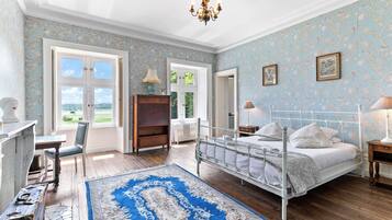 Un dormitorio con una cama grande, un escritorio, una silla y vistas al exterior a través de una ventana.