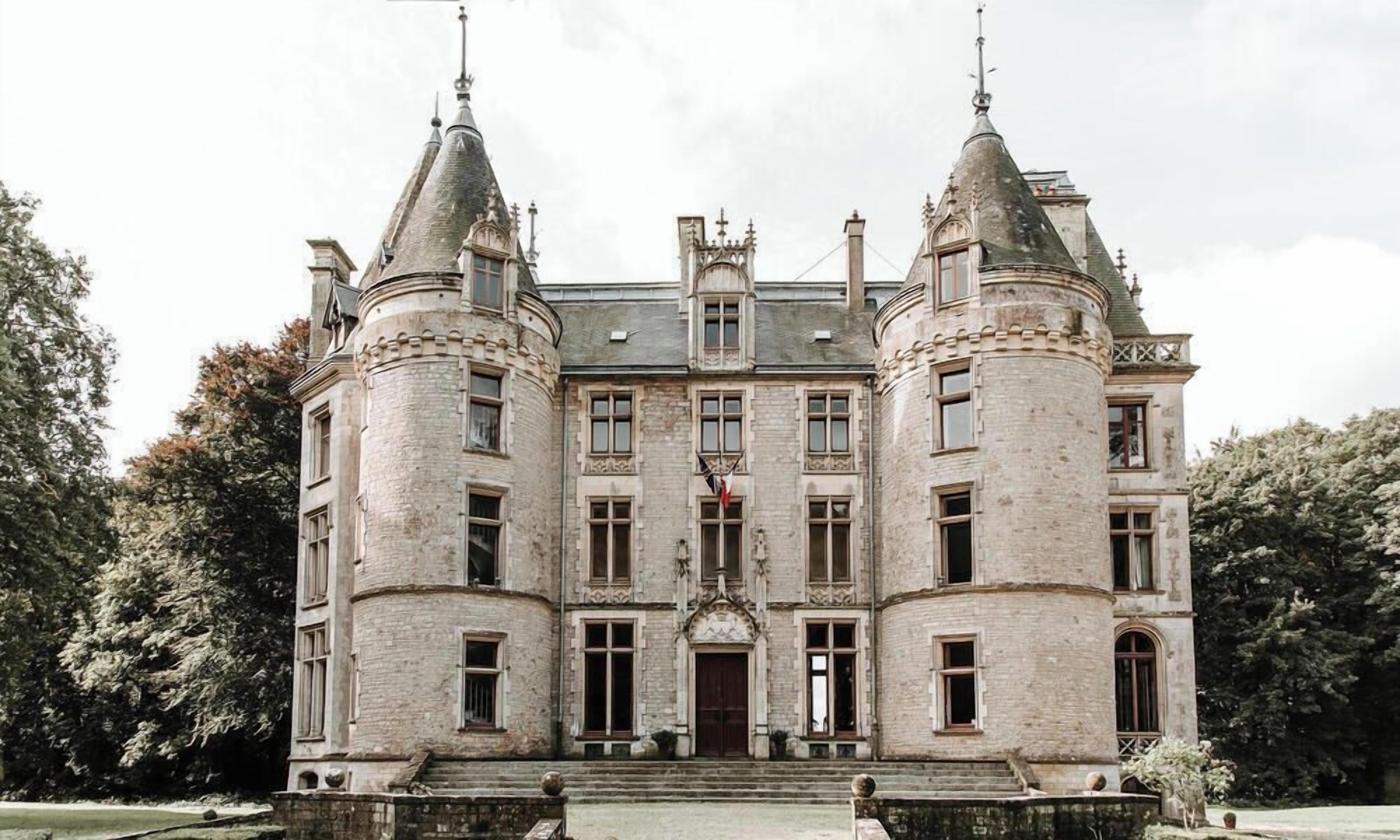A historic building with a central entrance, flanked by two towers, and a symmetrical facade with evenly spaced windows.