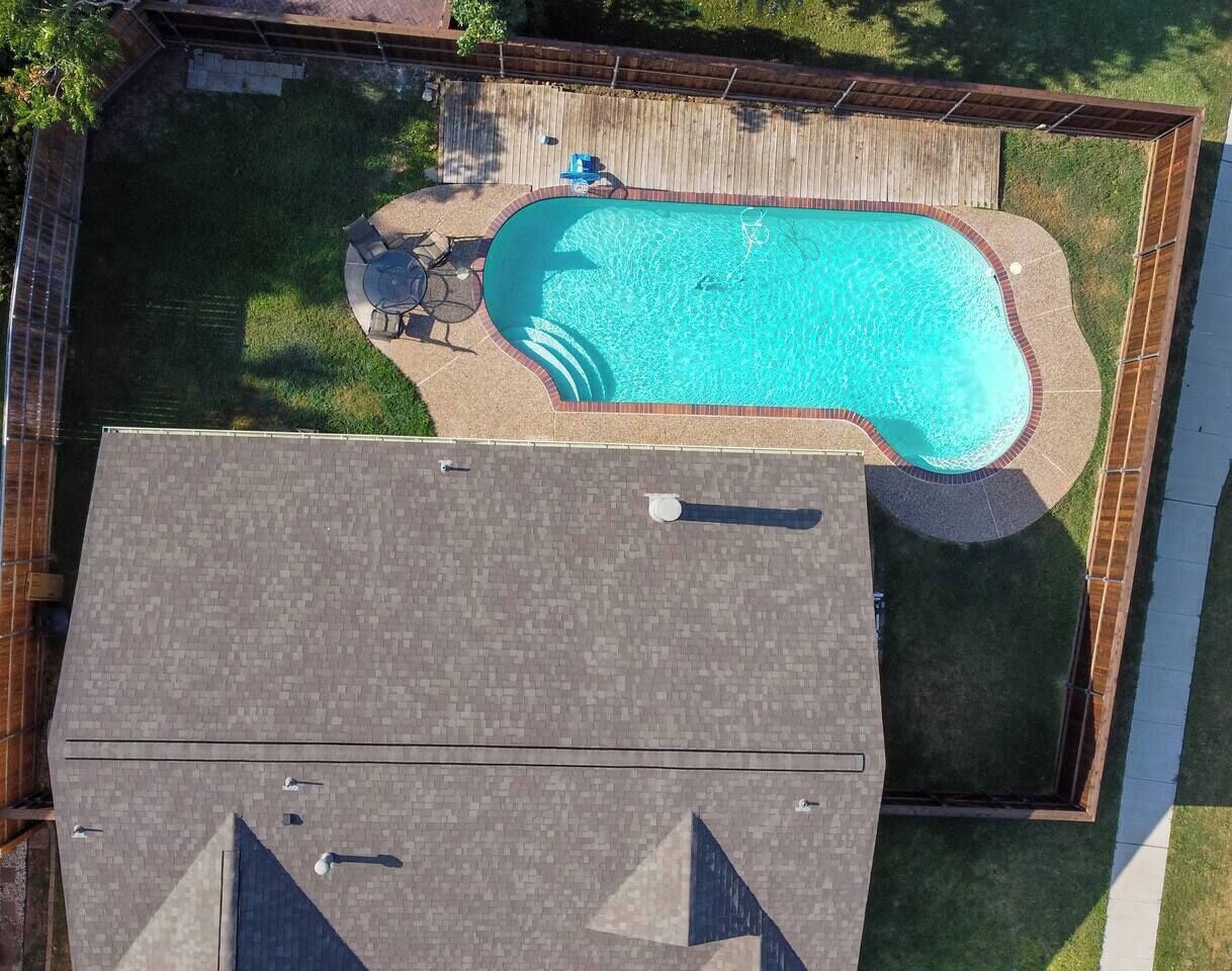 Una piscina residencial amb terrassa, envoltada per una tanca de fusta, i una zona de terrassa coberta amb mobles d'exterior.