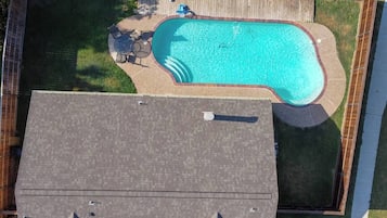 Una piscina residencial amb terrassa, envoltada per una tanca de fusta, i una zona de terrassa coberta amb mobles d'exterior.