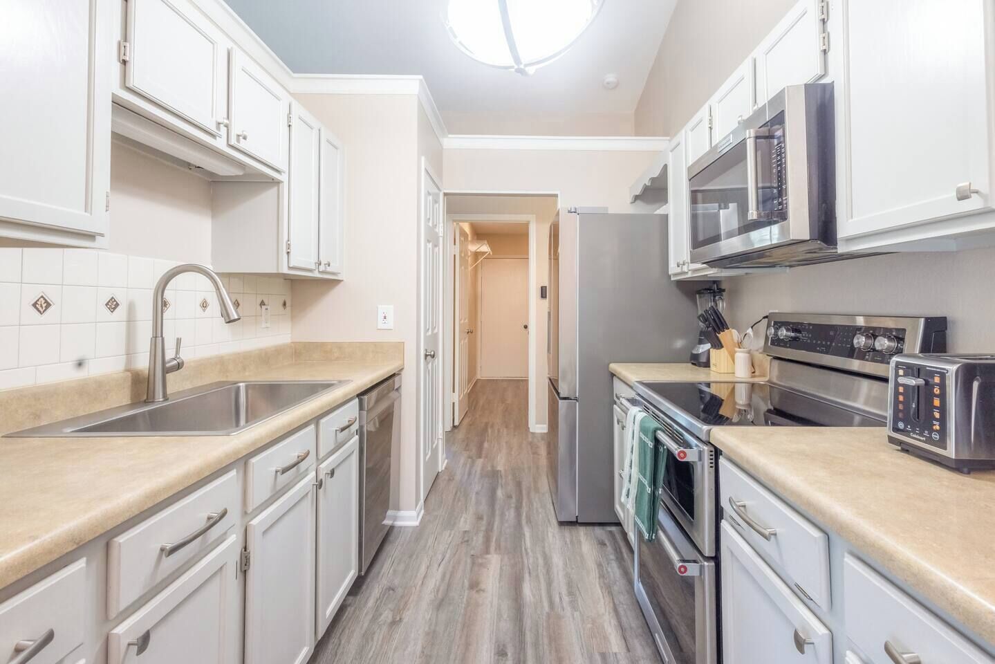 A modern kitchen with white cabinetry, stainless steel appliances, and a wooden floor.