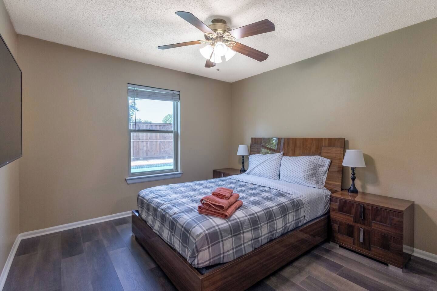 Quarto com cama, mesas de cabeceira, ventilador de teto, janela e vista para o exterior.